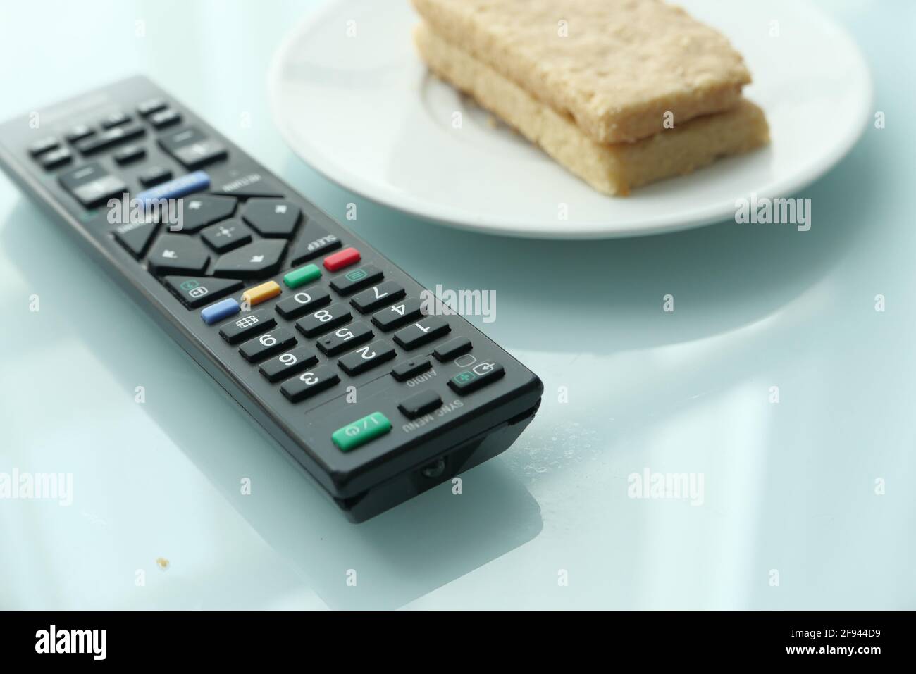 close up of tv remote and cookies on pate on table  Stock Photo