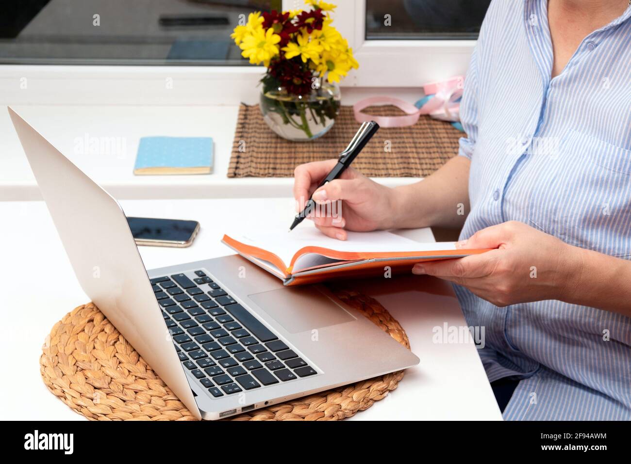 A woman makes notes in a notebook while sitting at a laptop. Selective focus. Stock Photo