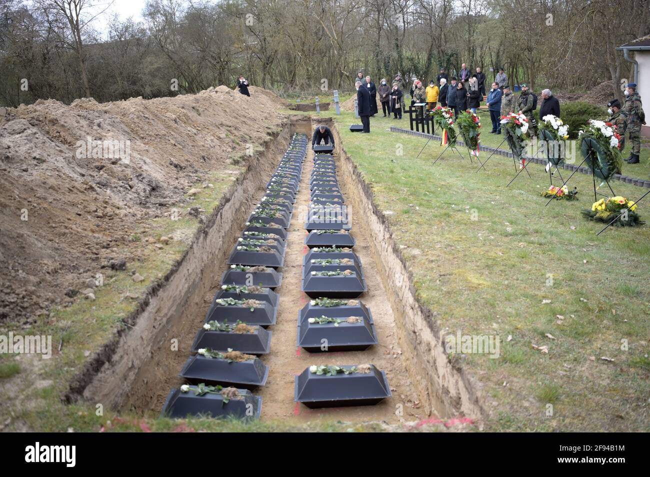 Brandenburg, Lietzen: 16 April 2021, Joachim Kozlowski, reburier at the  Volksbund Deutsche Kriegsgräberfürsorge e.V., places one of the coffins on  the bottom of the pit during the burial of 120 fallen German