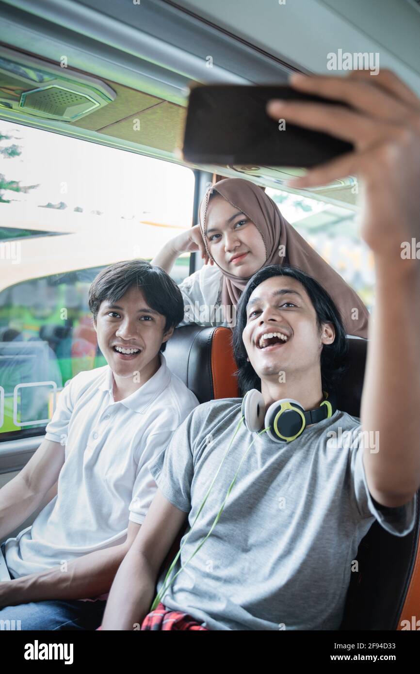 Three friends smile and pose in front of their cellphone camera while taking selfies together Stock Photo