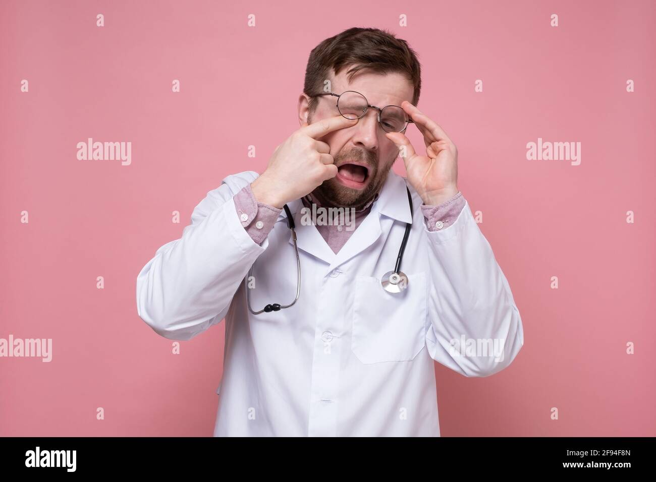 Tired, sleepy doctor with a stethoscope around neck raised glasses and