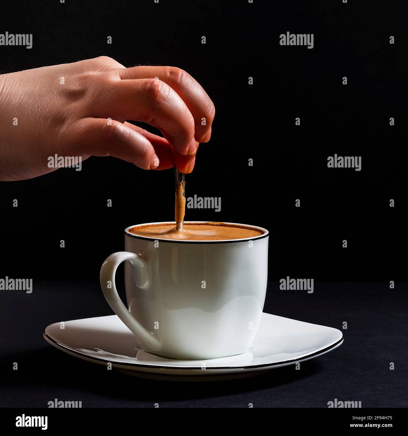 Woman's hand stirring a latte.This is a square-format photo taken on a black background under artificial light in a studio. Stock Photo