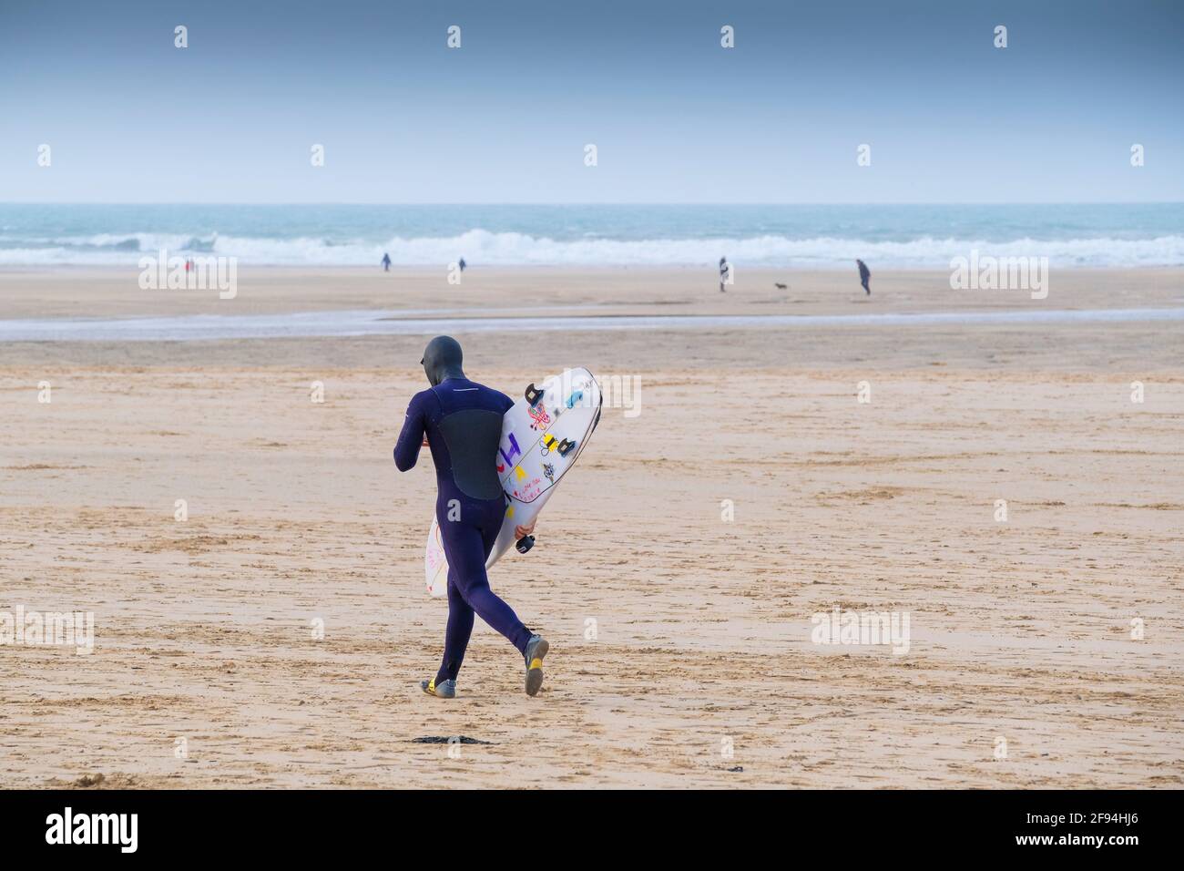 A surfer carrying his surfboard and running across Crantock Beach in Newquay in Cornwall. Stock Photo