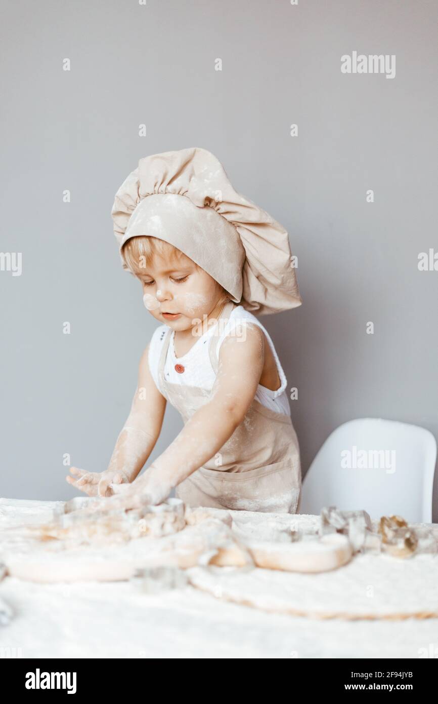 a happy child in an apron and a chef's hat prepares dough, bakes cookies in the kitchen Stock Photo