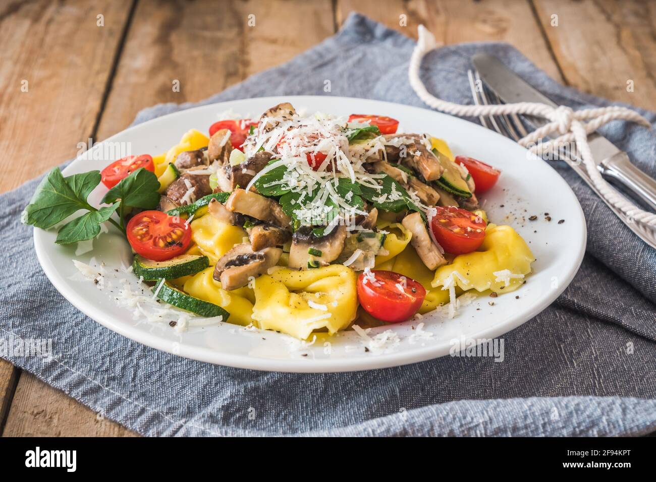 Italian cuisine: Tortellini with vegetarian mushroom cream sauce, zucchini,  fresh cherry tomatoes and parmesan cheese on a rustic wooden table Stock Photo