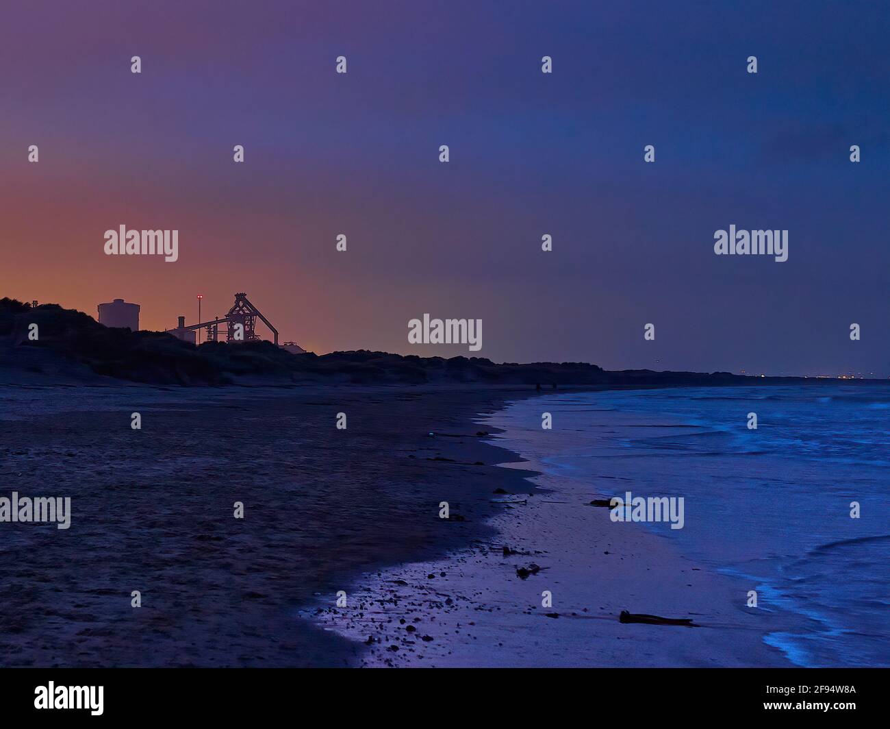 A panoramic sweep of Redcar Beach towards South Gare at twilight, with the last of the sunset silhouetting the skeletal Steelworks. Stock Photo