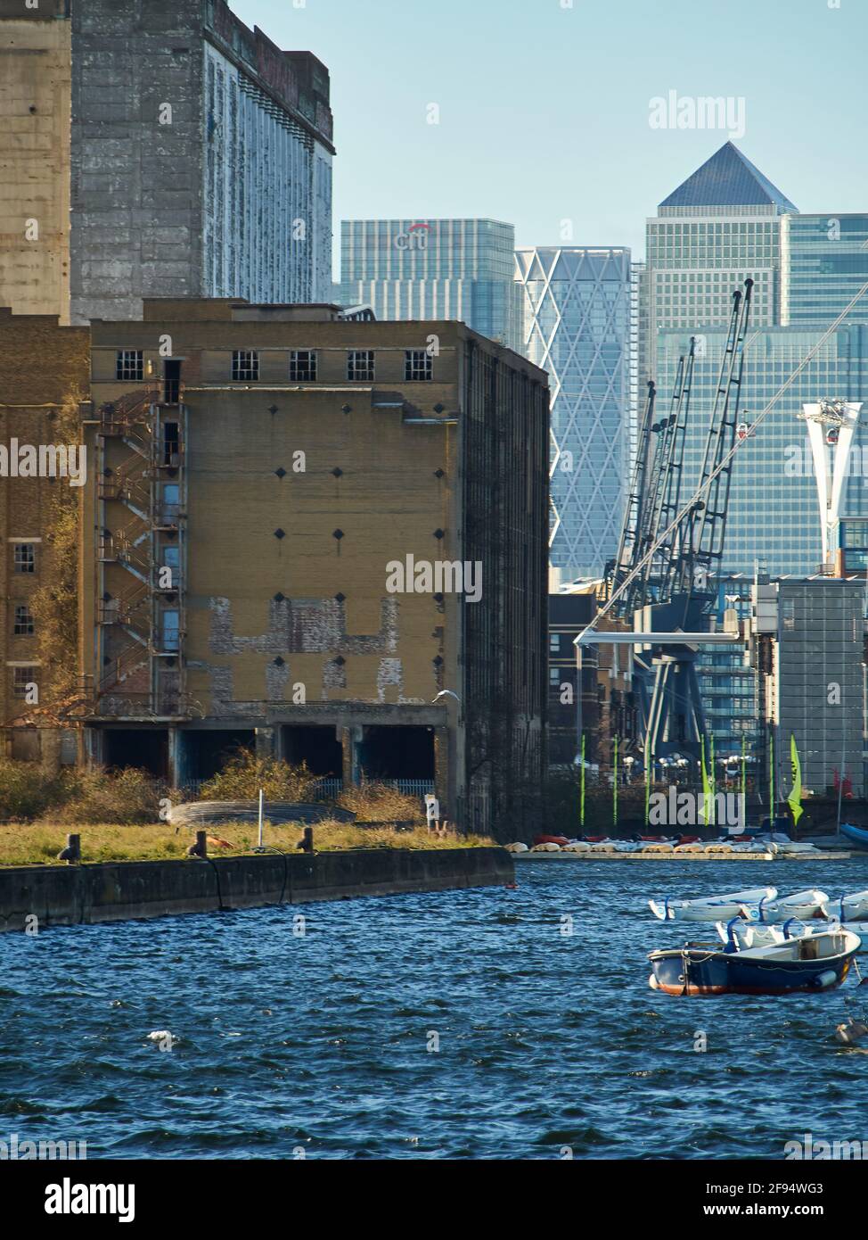 London UK, Dec 2019 - Old and new together, the derelict hulk of the old Millennium Mills warehouses and the sleek, modern towers of Canary Wharf. Stock Photo