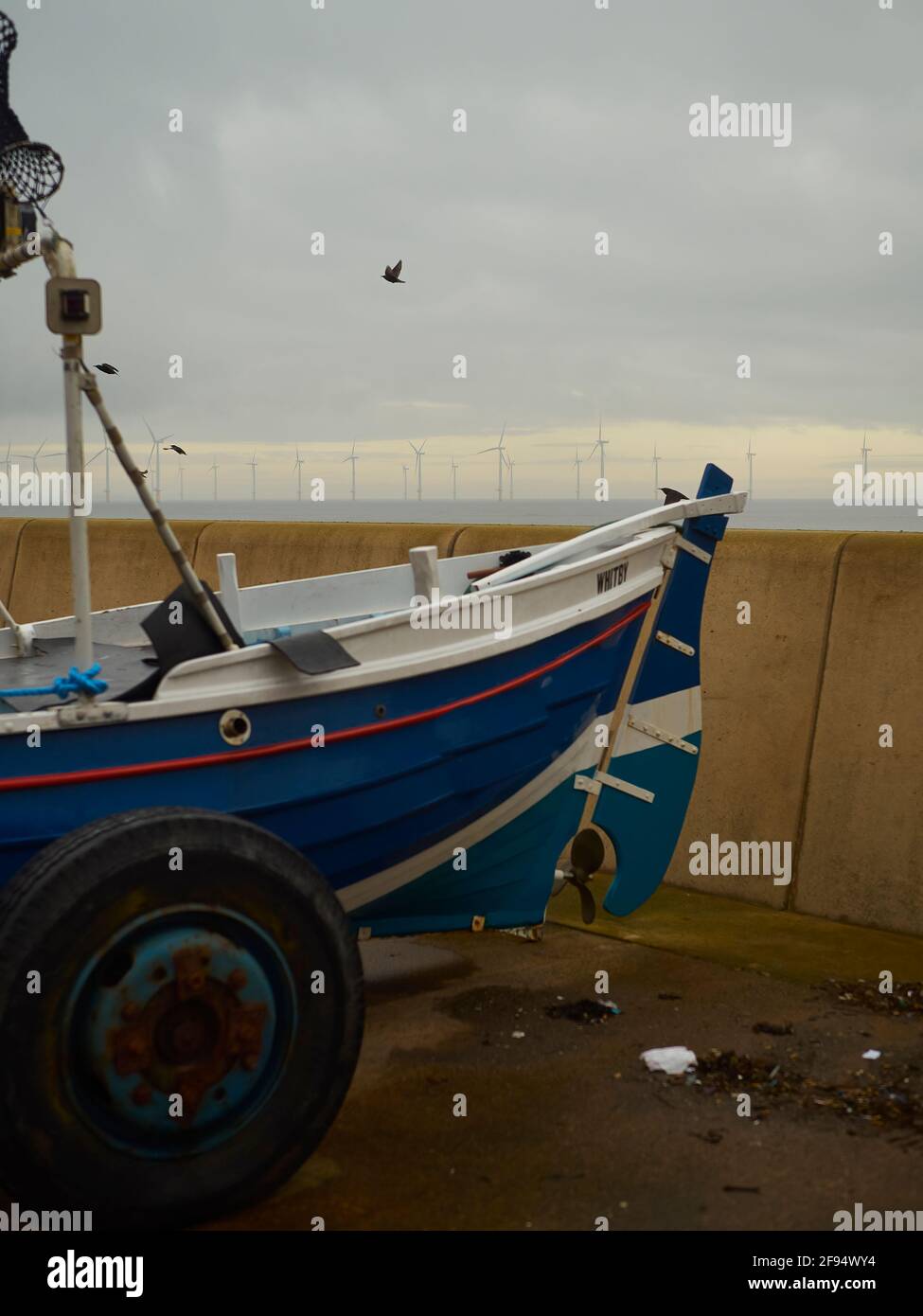 Redcar UK, Dec 2018 - Old and new, a traditional Yorkshire Cobble fishing boat with a modern wind farm on the horizon. A bird on the breeze gives life Stock Photo