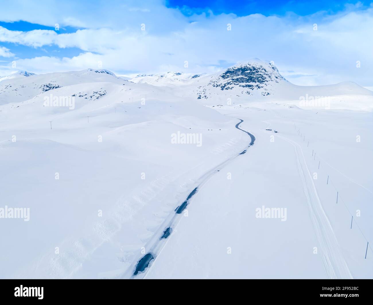 Lonely frozen road winding through a snow covered mountain landscape. Stock Photo