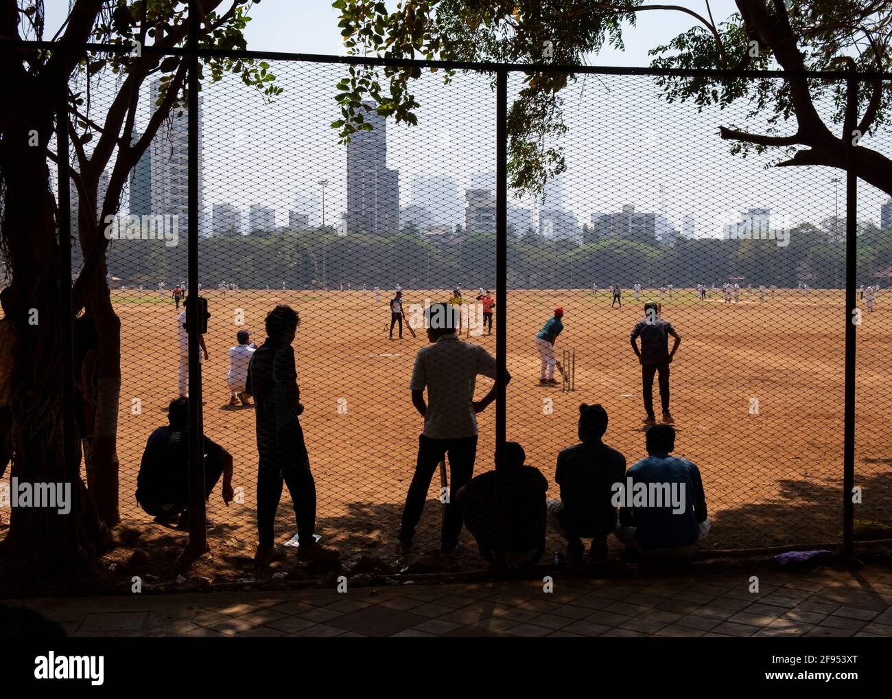 Silhouette of teenagers standing behind a fence watching a cricket match in Shivaji Park in Mumbai-Dadar,Maharashtra, India Stock Photo