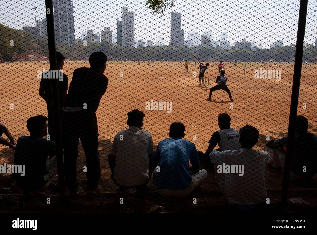 Silhouette of teenagers standing behind a fence watching a cricket match in Shivaji Park in Mumbai-Dadar,Maharashtra, India Stock Photo