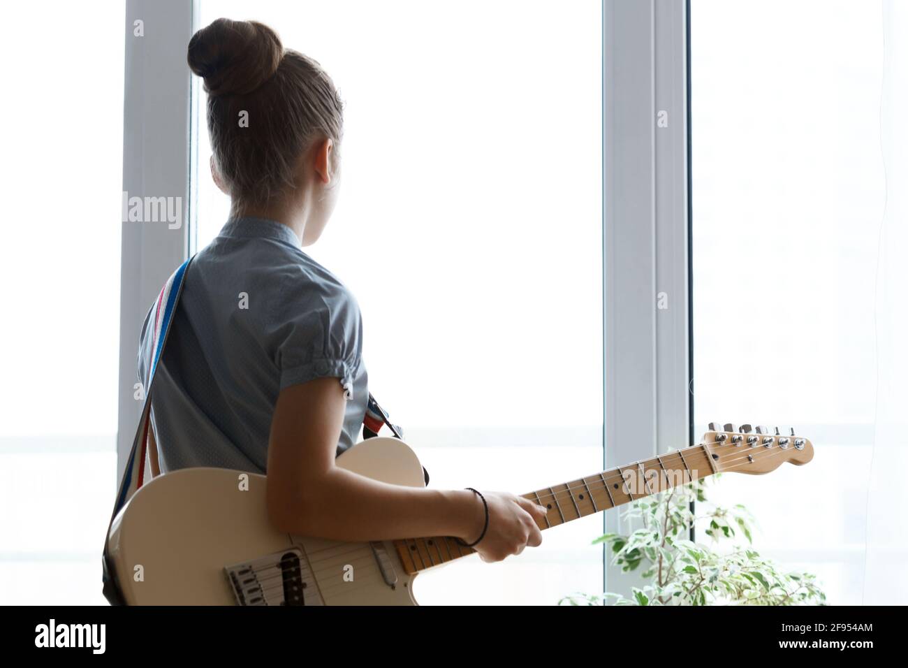 Silhouette of a beautiful young girl with a guitar near the window. Stock Photo