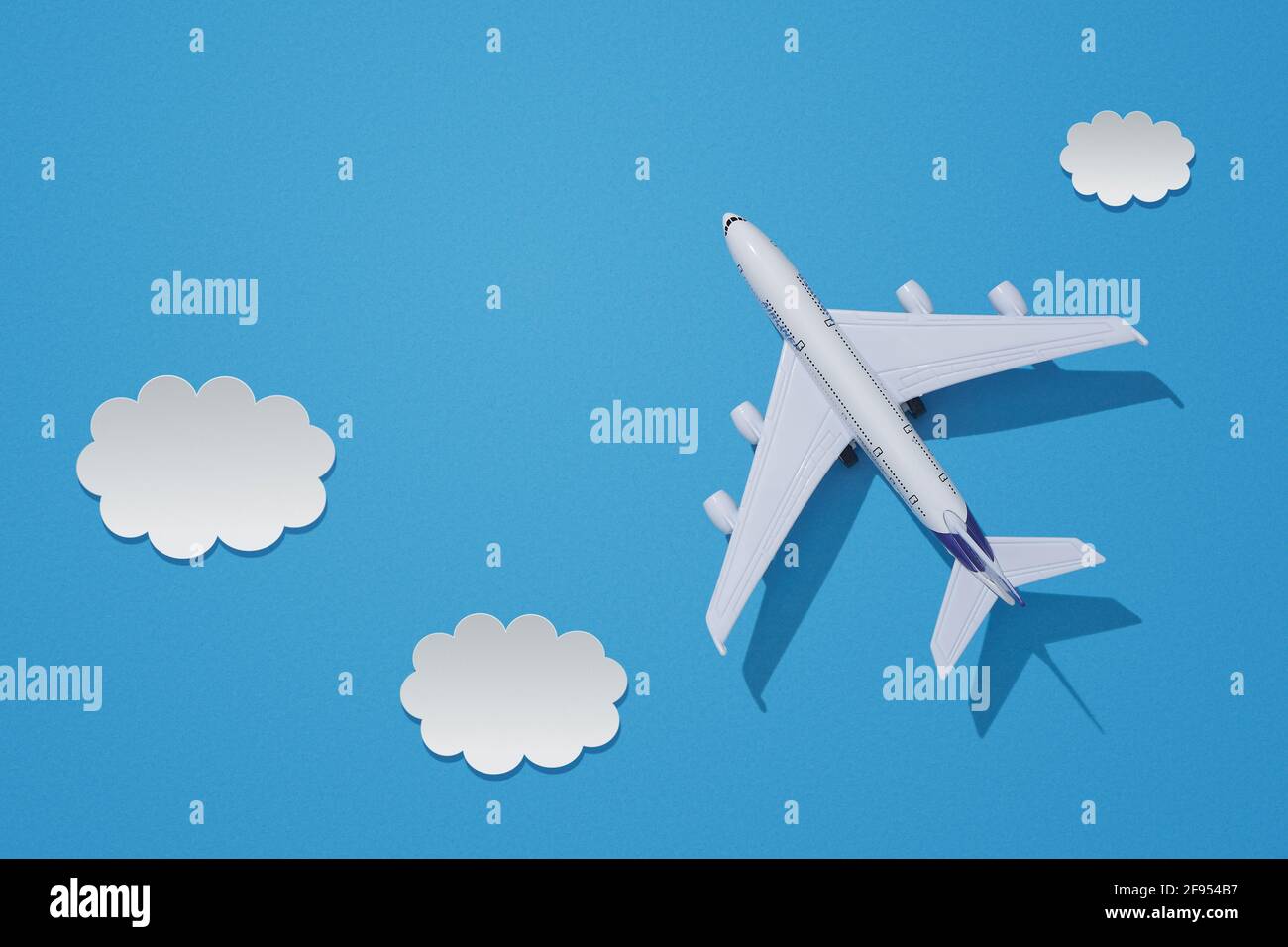 Miniature toy airplane on colorful paper background. Flat lay design of travel concept with plane and clouds on blue sky with copy space. Stock Photo