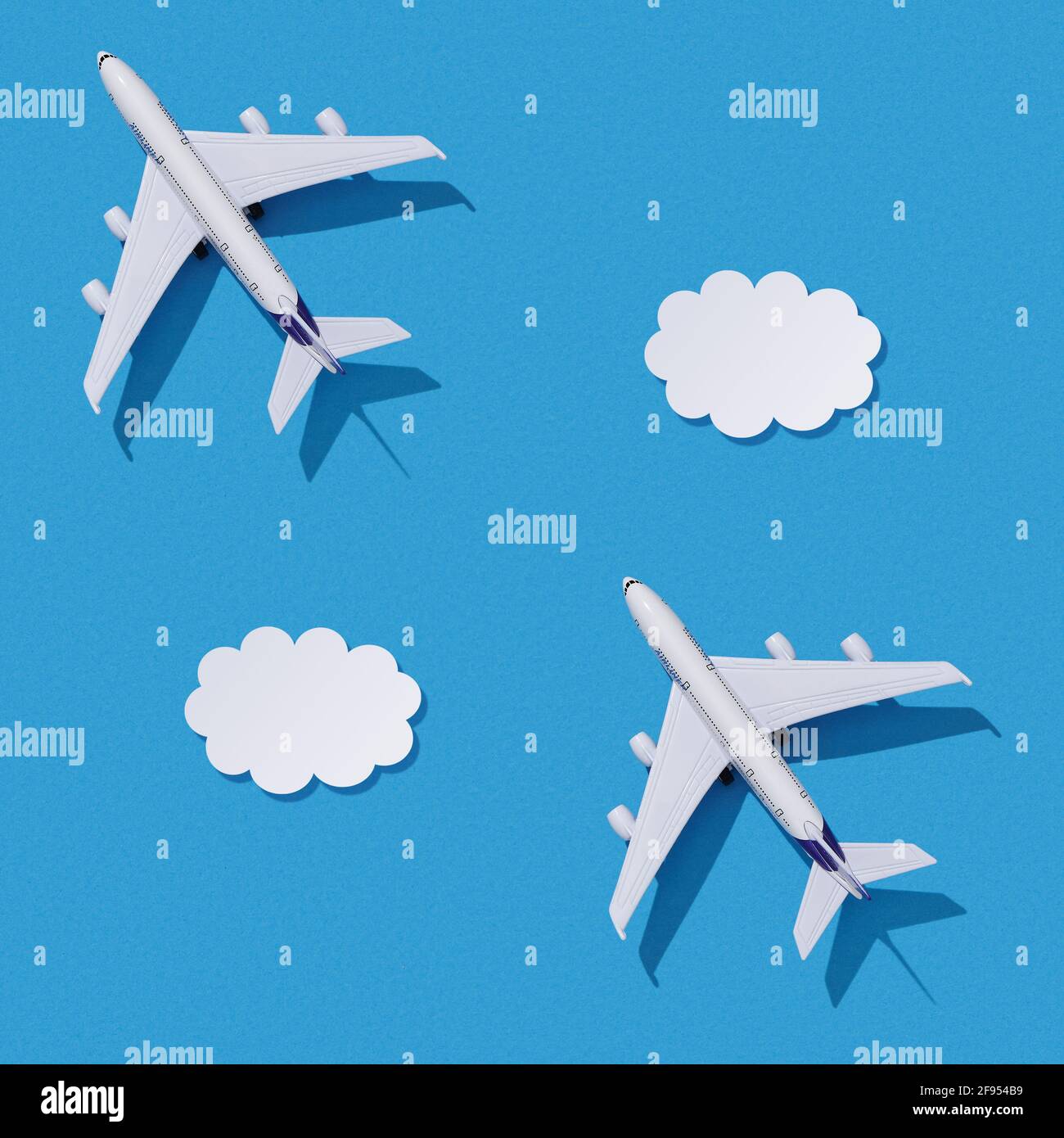 Miniature toy airplane on colorful paper background. Flat lay design of travel concept with plane and clouds on blue sky. Seamless texture. Stock Photo