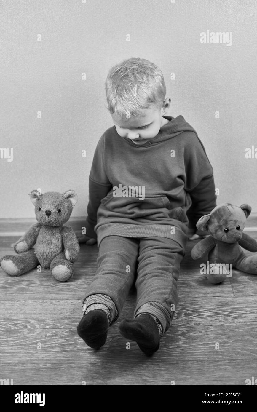 A threeyearold caucasian boy sits alone on the floor next to teddy bears, the theme of child