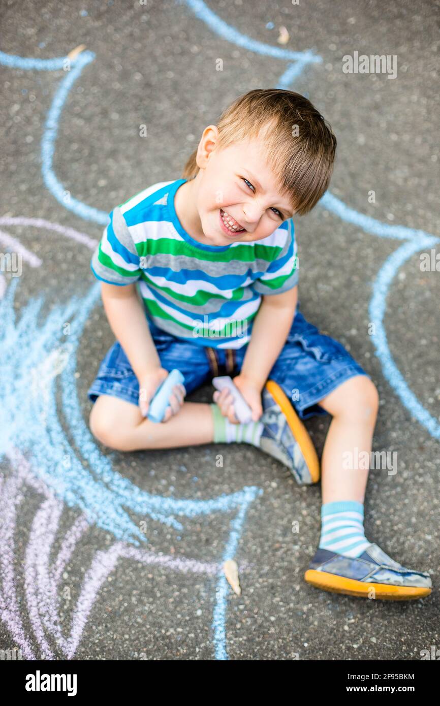 Cute boy and girl drawing with chalk on the sidewalk in the park ...