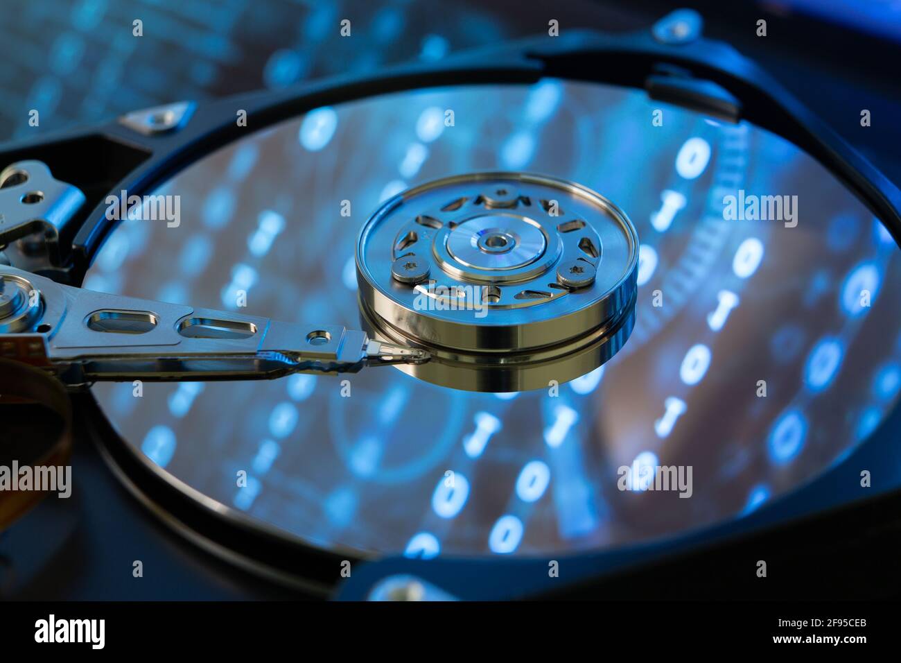 Inside of a hard disk HDD with binary code, zeros and ones, projected onto the surface. Bluish appearance. Stock Photo