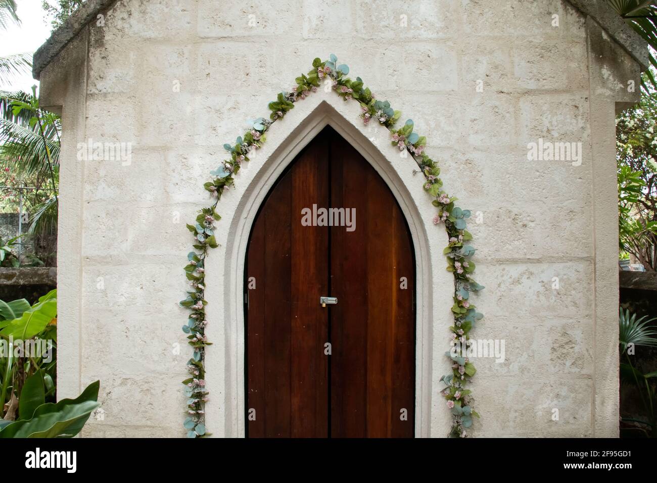 A slightly ajar old-fashioned medieval frame door in Barbados, surrounded by climbing green ivy vines with blossoms and old-fashioned colonial chapel. Stock Photo