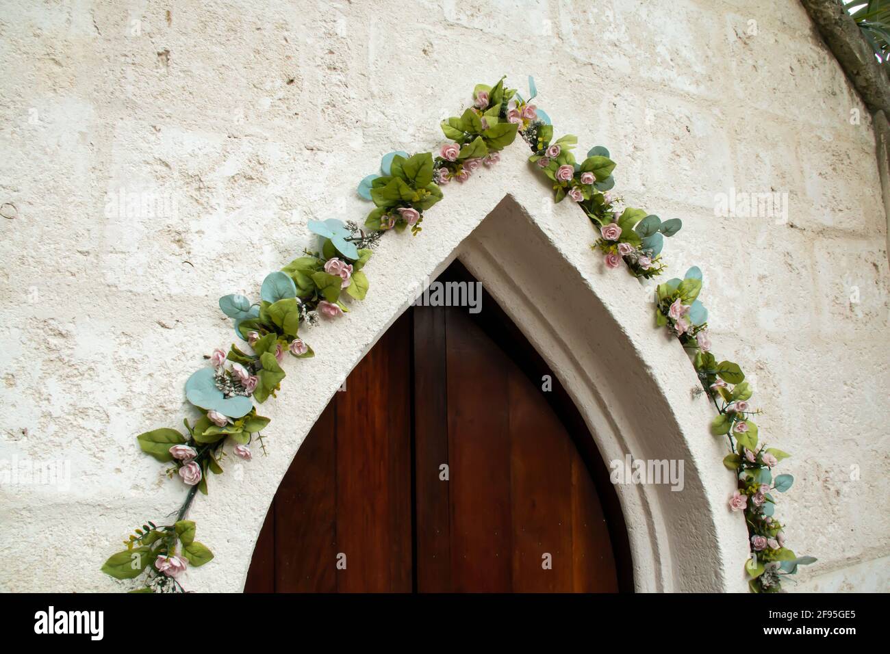 A slightly ajar old-fashioned medieval frame door in Barbados, surrounded by climbing green ivy vines with blossoms and old-fashioned colonial church. Stock Photo