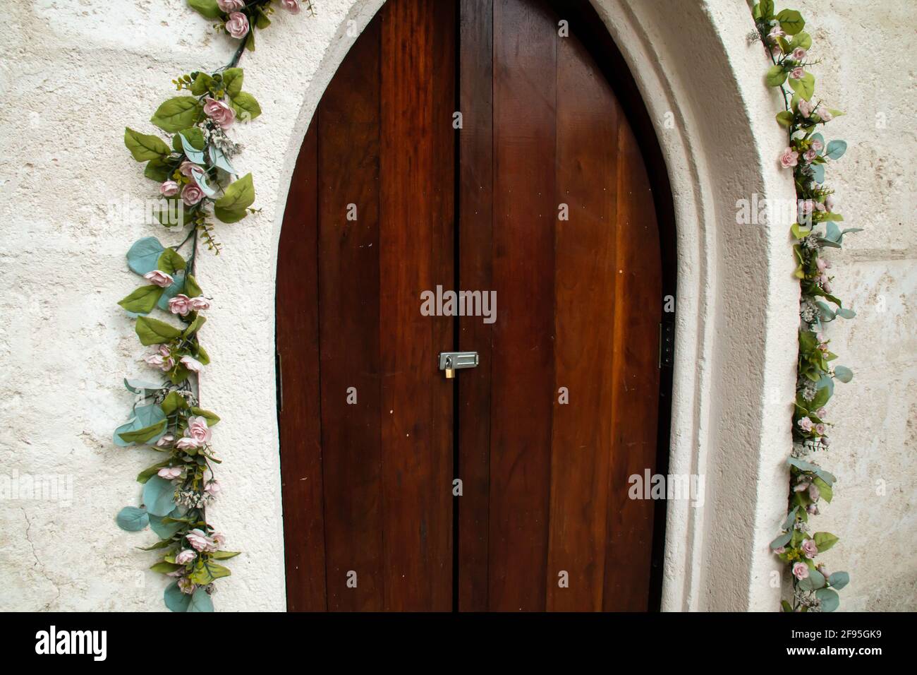 A slightly ajar old-fashioned medieval frame door in Barbados, surrounded by climbing green ivy vines with blossoms and old-fashioned colonial chapel. Stock Photo