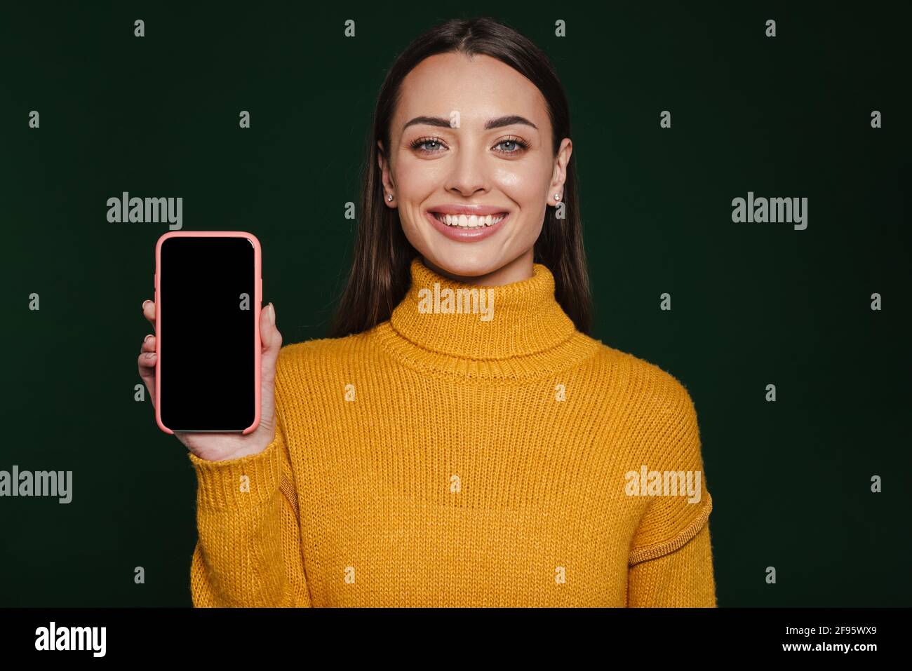 Joyful beautiful girl smiling and showing mobile phone isolated over green background Stock Photo