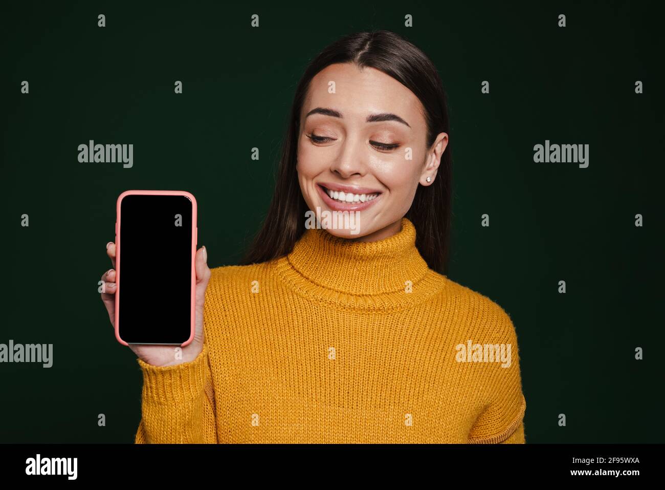 Joyful beautiful girl smiling and showing mobile phone isolated over green background Stock Photo