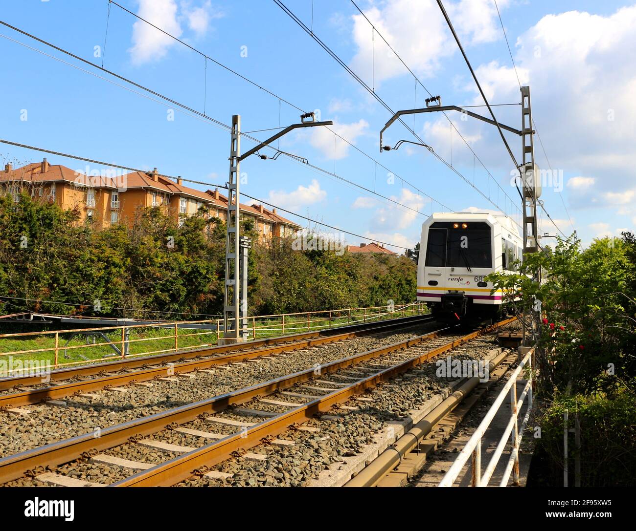 Spanish commuter train travelling at speed with overhead electric cables through urban