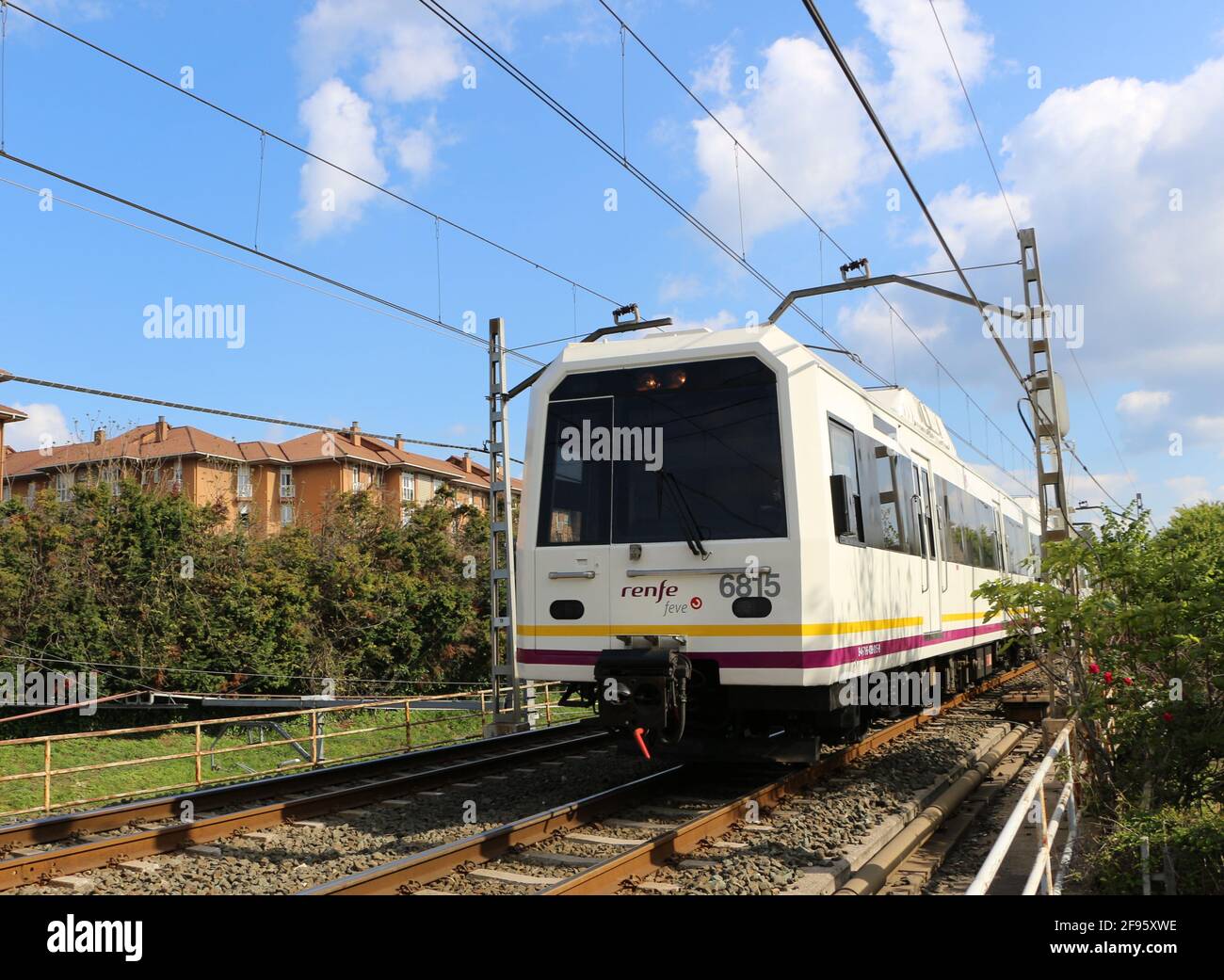 Spanish commuter train travelling at speed with overhead electric cables through urban