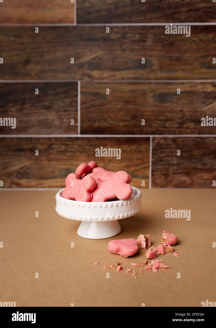Pink dog treats on white mini cake stand against brown wooden backdrop Stock Photo
