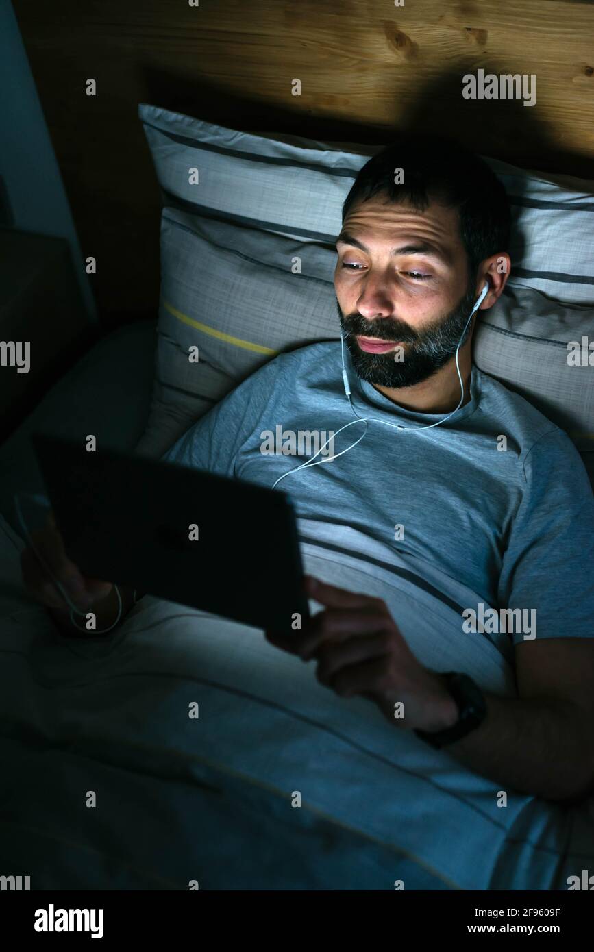 Man lying on bed with tablet in darkness Stock Photo