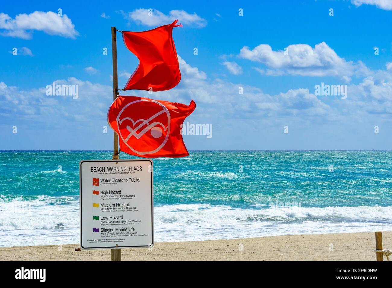 Water Closed to Public red warning flags and informational sign in front of rough, choppy ocean - Hollywood, Florida, USA Stock Photo