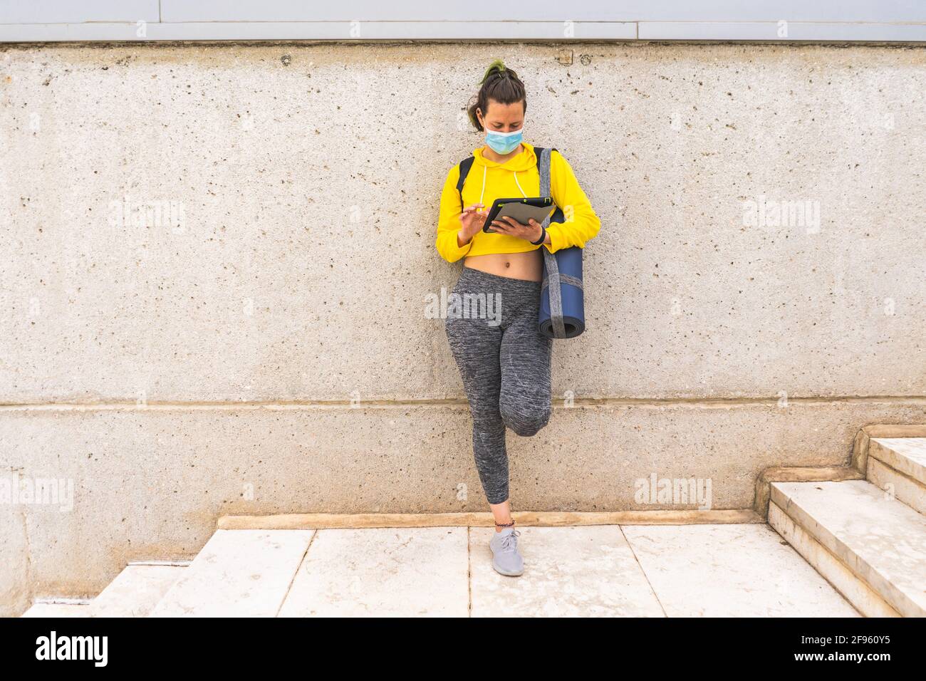 Active woman with sportswear tablet and mask waiting on stairs Stock Photo