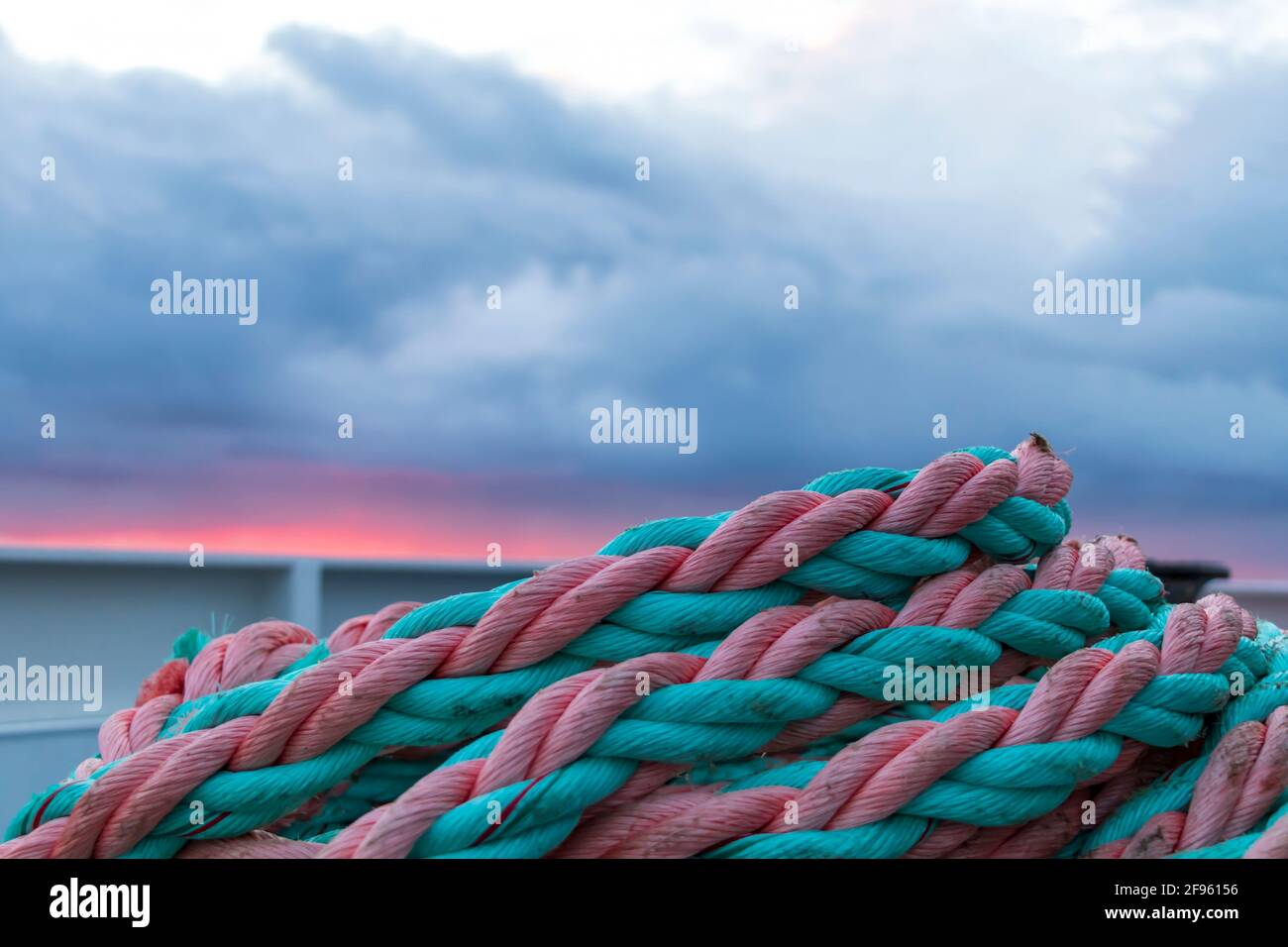 Nautical background. Colorful rope knot on the boat in beautiful moody light. Closeup of an old pink green frayed boat rope on sunrise with dramatic s Stock Photo