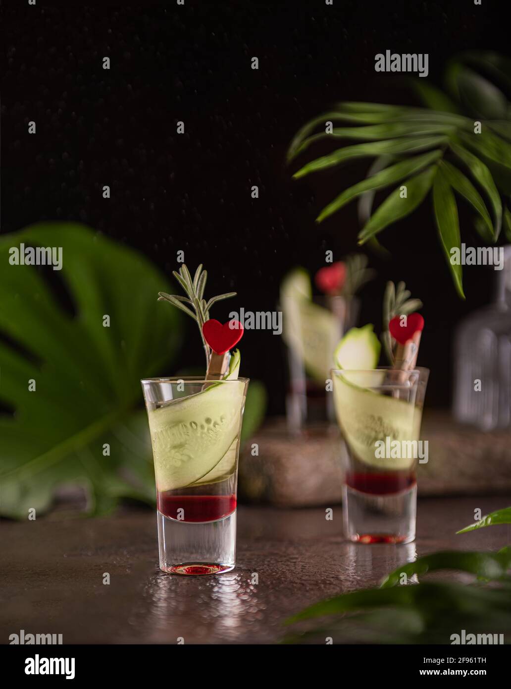 Layered shots with red grenadine and vodka decorated with slices of cucumber, fresh rosemary and red hearts. Still life with alcohol cocktails and tro Stock Photo