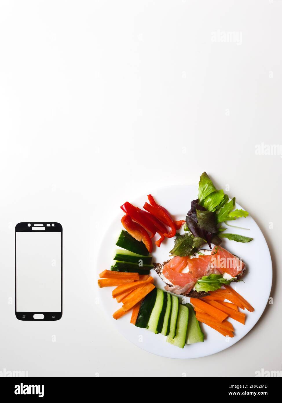 smartphone frame & white plate with vegetables & salmon on white table Stock Photo