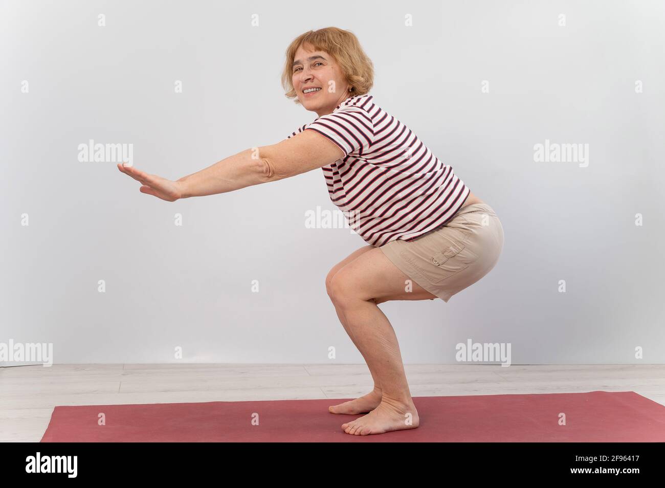Elderly woman doing squats on a white background. The old lady is doing