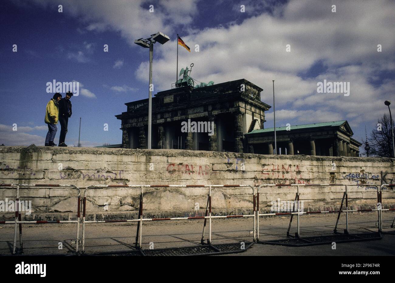 Zwei Touristen gehen am Brandenburger Tor auf dem Rest der Berliner Mauer spazieren - two tourists take a stroll on the remains of the Berlin Wall at the Brandenburg Gate. Stock Photo