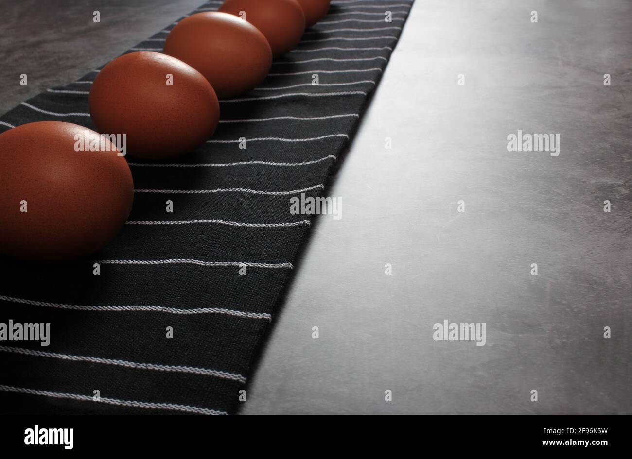 Easter concept. Eggs against black striped kitchen towel on dark background. Copy space. Close up. Stock Photo