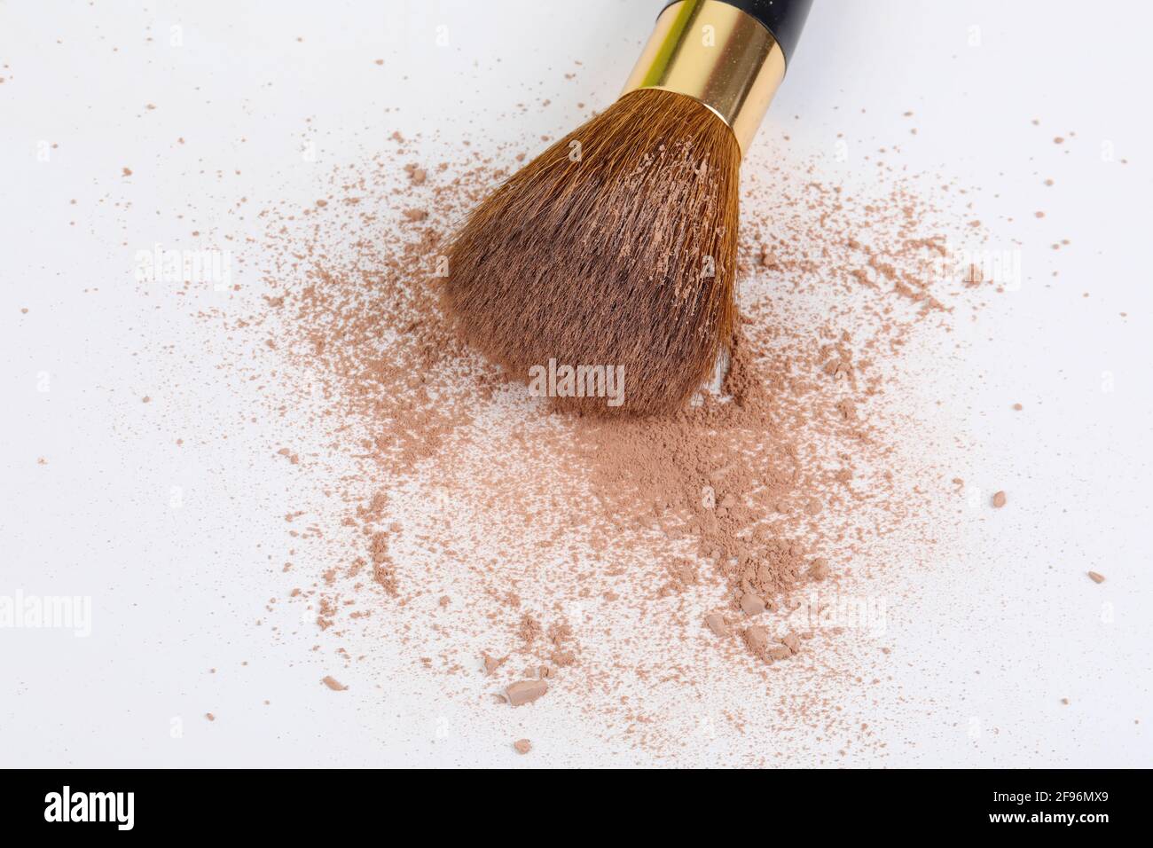 Scattered tan colored facial loose powder and make-up brush isolated on white background. Copy space. Stock Photo