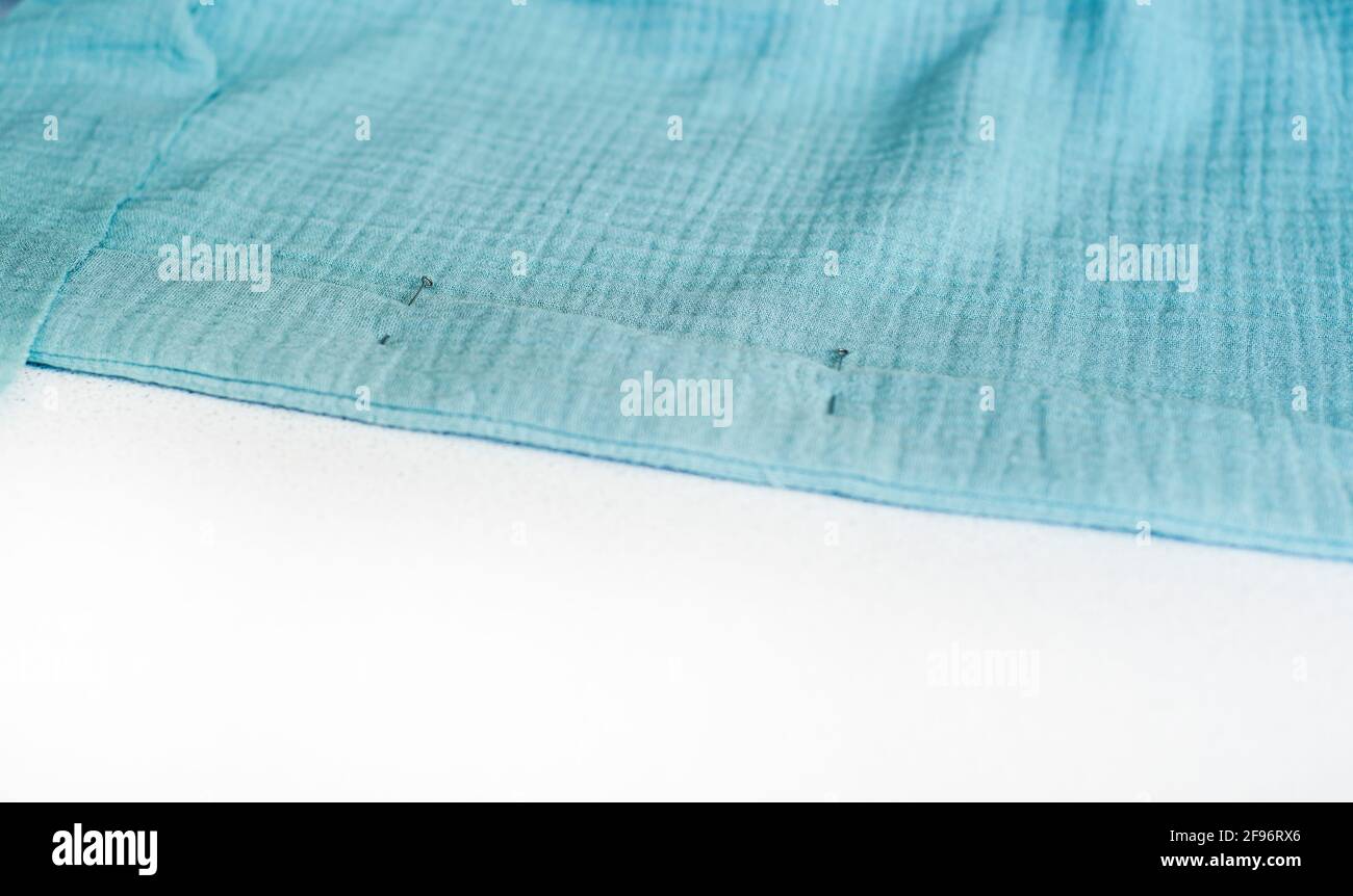 Sewing Turquoise Cotton. Metal pins will pin the hem of the fabric. White background for copy space. Sewing themes. Stock Photo