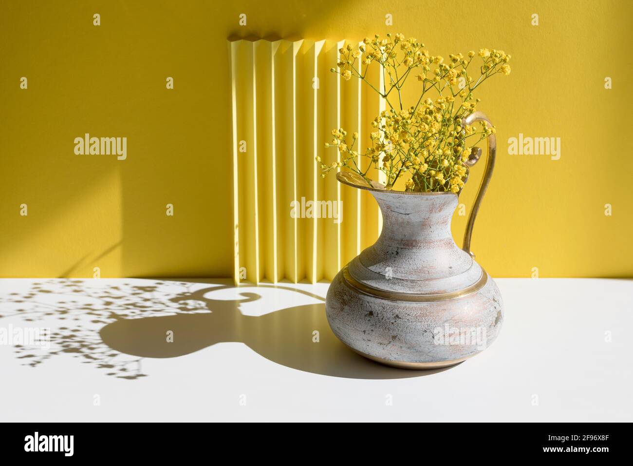 A bouquet of Gypsophila in a brass jug with harsh shadow. Minimal interior decoration concept. Minimal summer concept. Copy space. Stock Photo