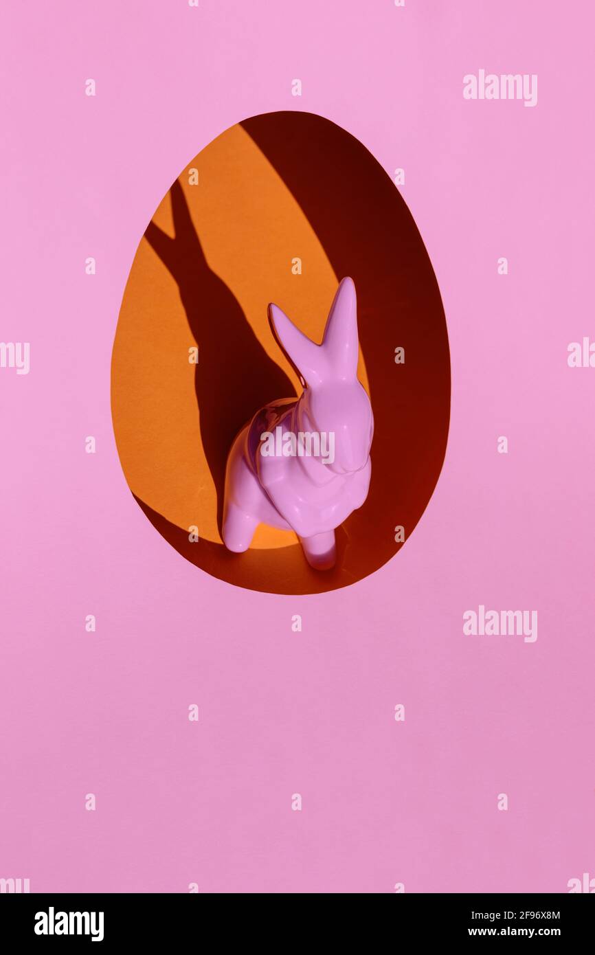 Minimalist Easter concept. Creative layout made with pink porcelain rabbit inside the orange egg on bright pink background. Copy space. Stock Photo