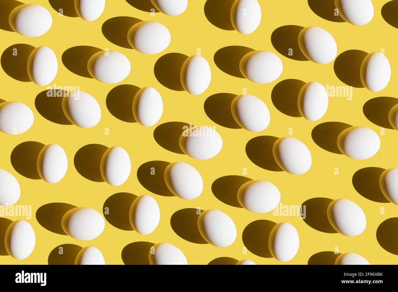 Seamless pattern with white eggs and trend summer shadows on yellow background. Minimal Easter or food concept. Flat lay. Stock Photo