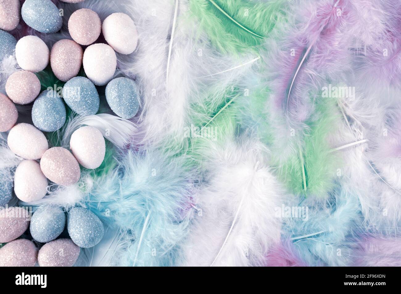 Happy Easter Holiday. Decorative Easter eggs on colorful feathers background. Copy space. Flat lay. Stock Photo