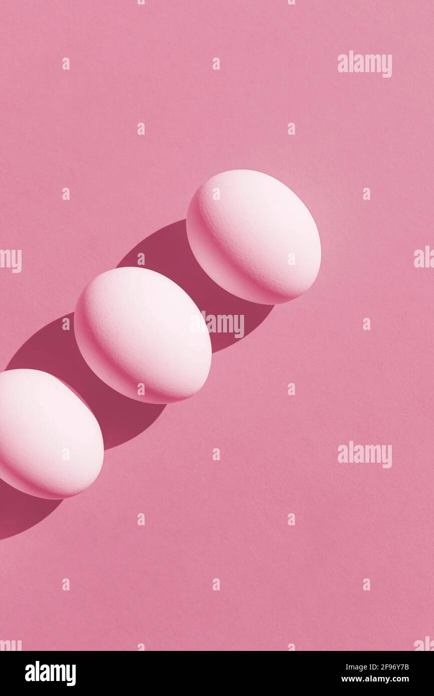 Easter Concept. White fresh eggs in isometric line on pink paper background. Minimal food concept. Vertical photo. Copy space. Flat lay. Stock Photo