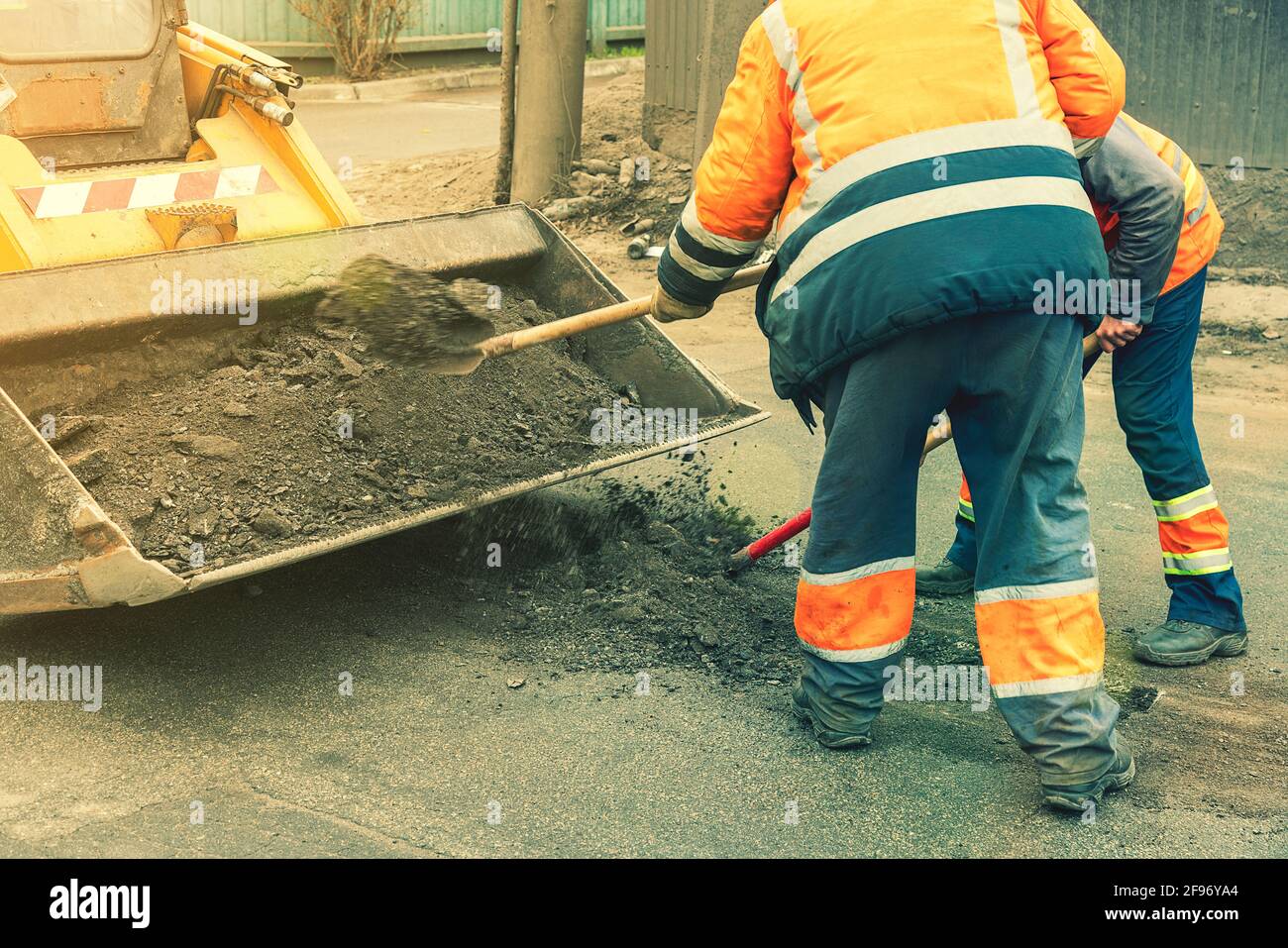 Road workers in bright orange reflective uniforms use shovels to scrape accumulated sand. maintenance of road and highway pavements. pothole repairing Stock Photo