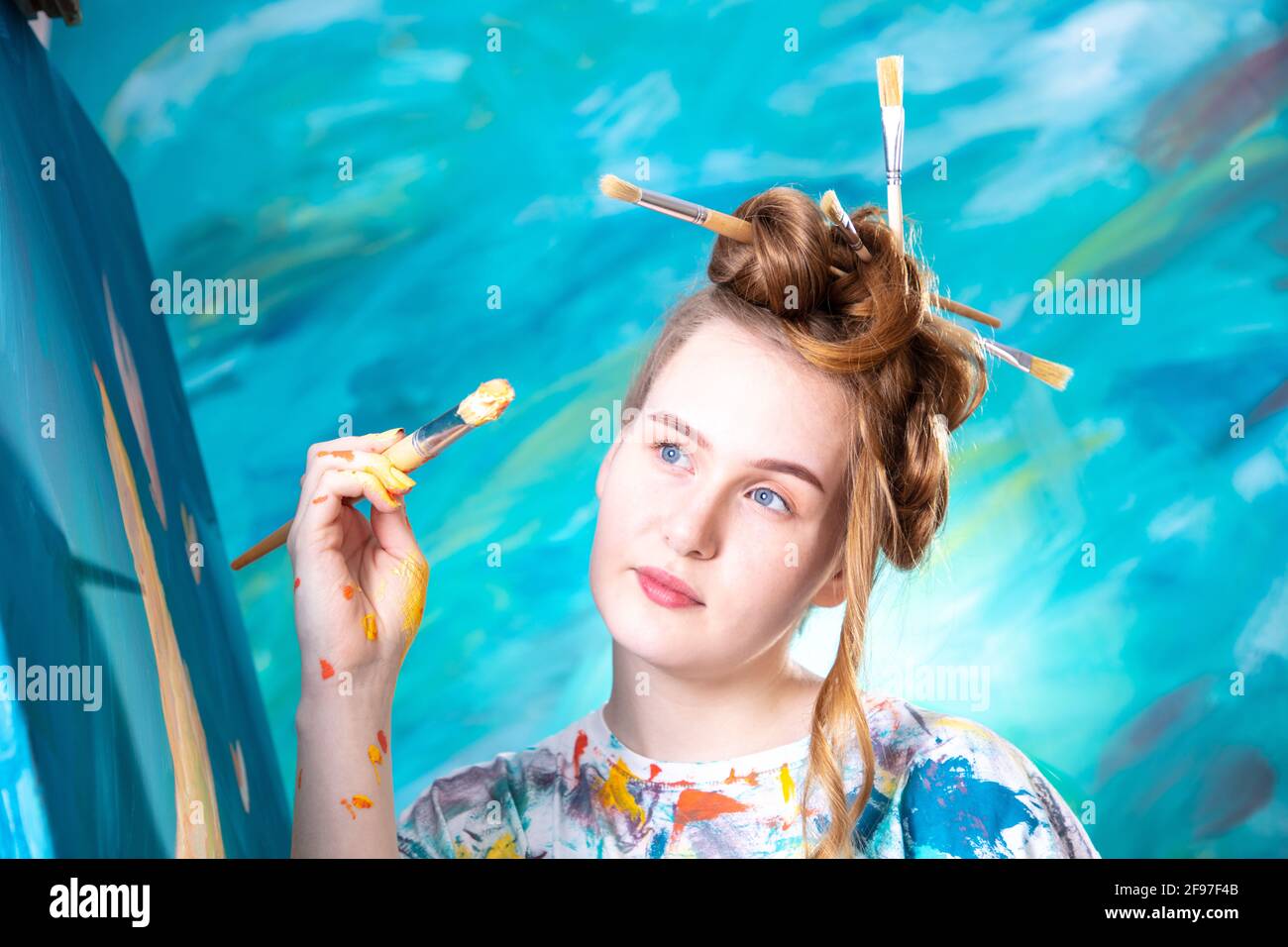 Young woman with updo and brush in her hair while painting. Stock Photo