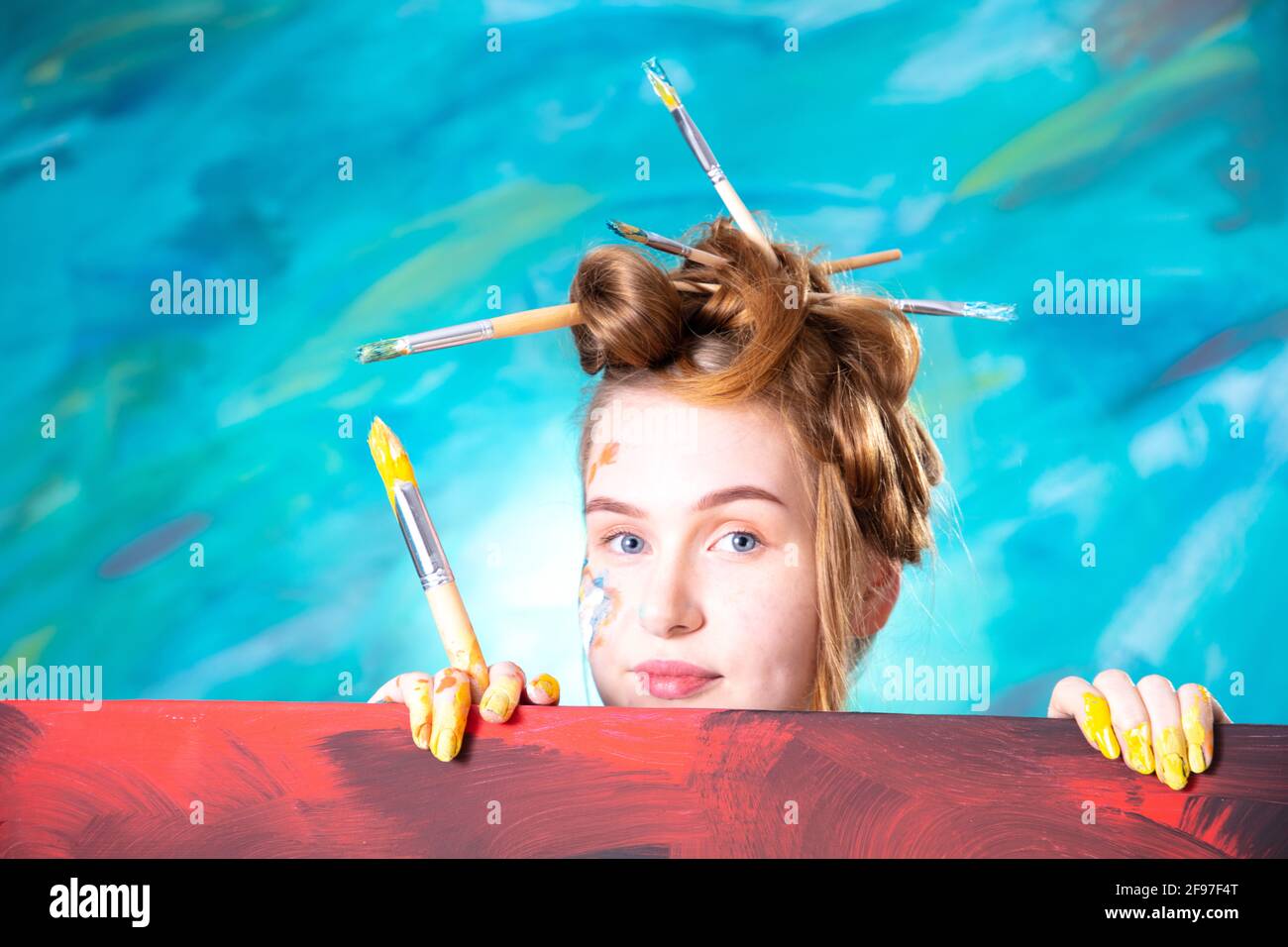 Young woman with updo and brush in her hair while painting. Stock Photo