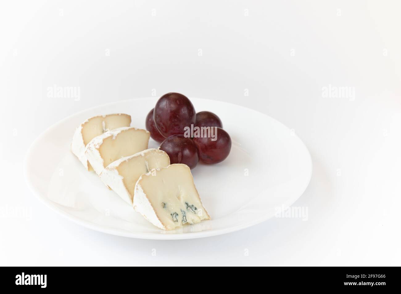pieces of camembert or brie cheese with red grapes on plate isolated on white background, soft cheese covered with edible white mold view from above, Stock Photo