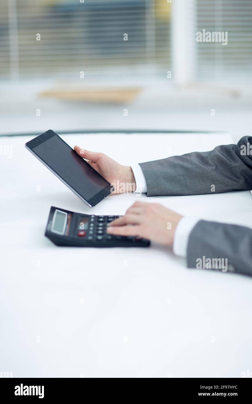 Manager Using Calculator Manager holds a tablet in his left hand in his right hand works on a ...